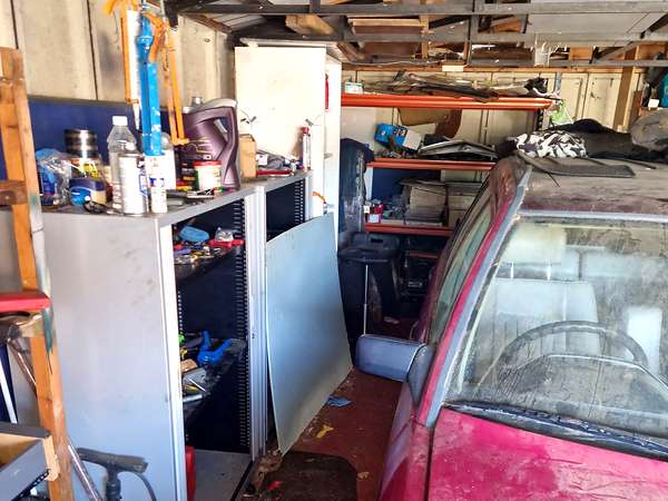 Packed double garage with a car inside, shelving and decades of stored belongings