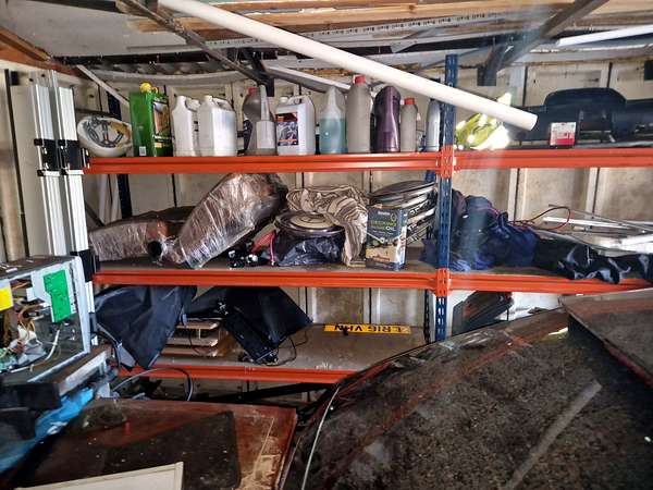 Racking stacked with oil cans, tools and stored goods in a garage