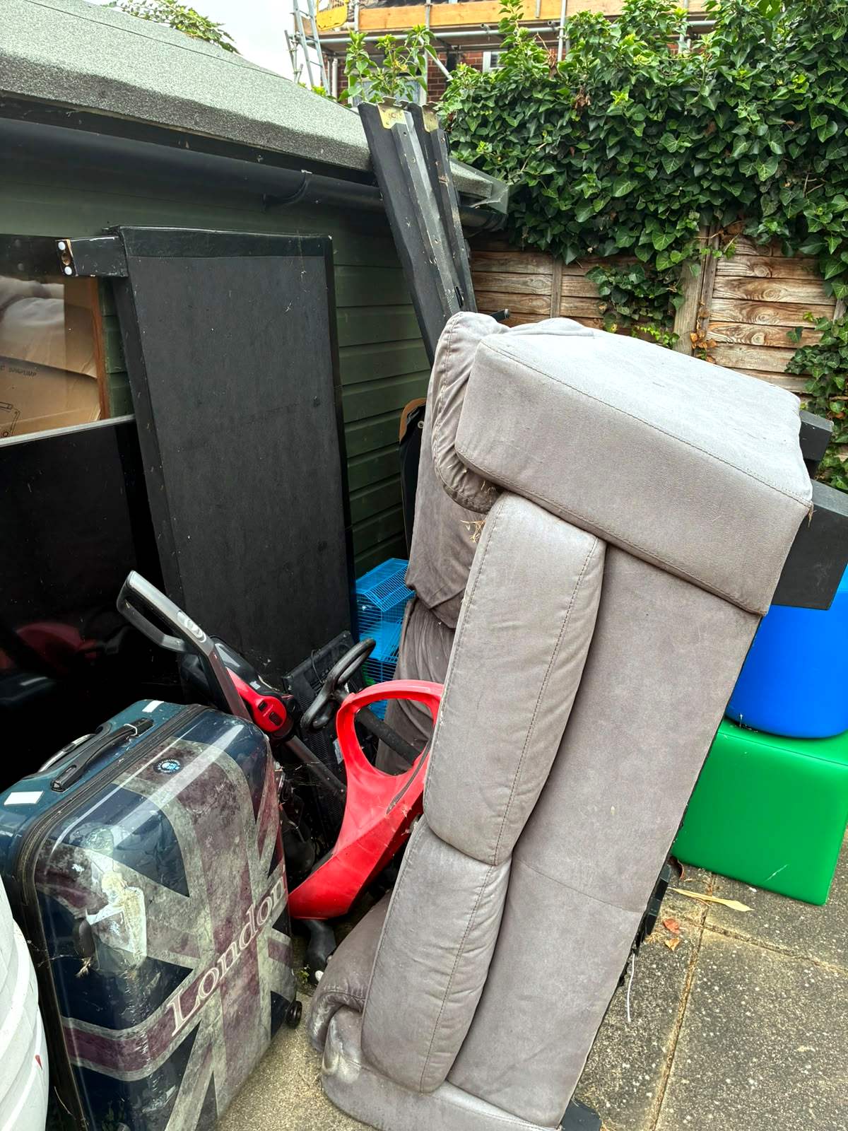 Old sofa and household junk stacked outside a garden shed before clearance