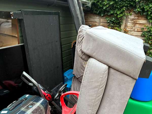 Old sofa and household junk stacked outside a garden shed before clearance